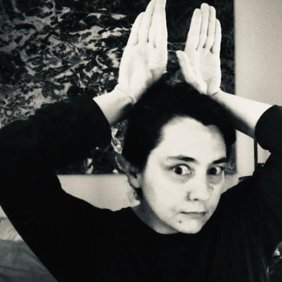 Black-and-white photograph: headshot with hands poised on top of head like rabbit ears. Cute face.